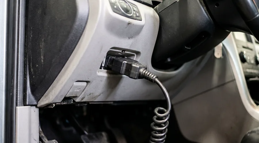 Diagnostic scan tool connector plugged into a vehicle's OBD-II port during electronic fault testing